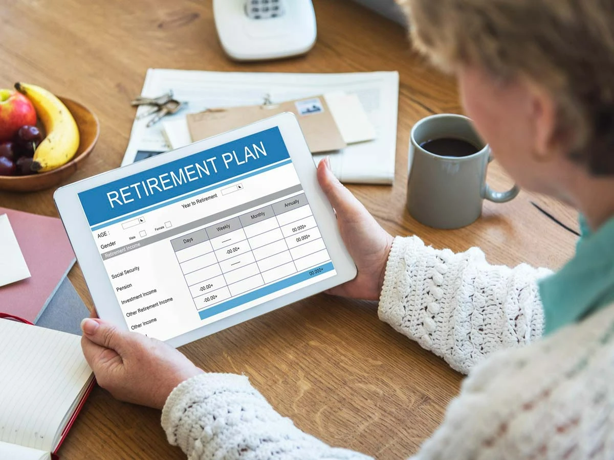 A person reviewing a retirement plan document on a digital tablet at a desk with coffee.