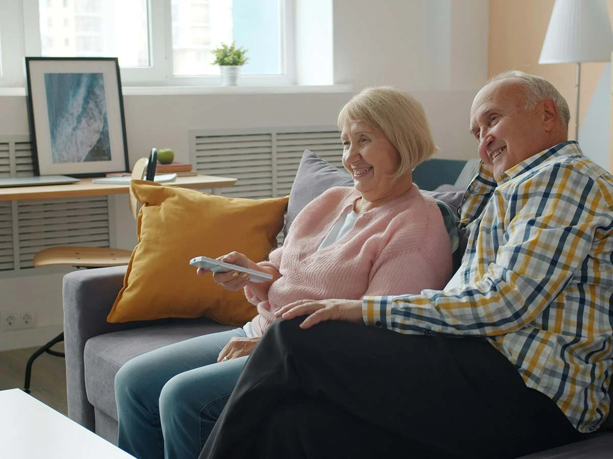 A happy senior couple sitting together on a sofa in their bright, modern new home after retiring abroad.