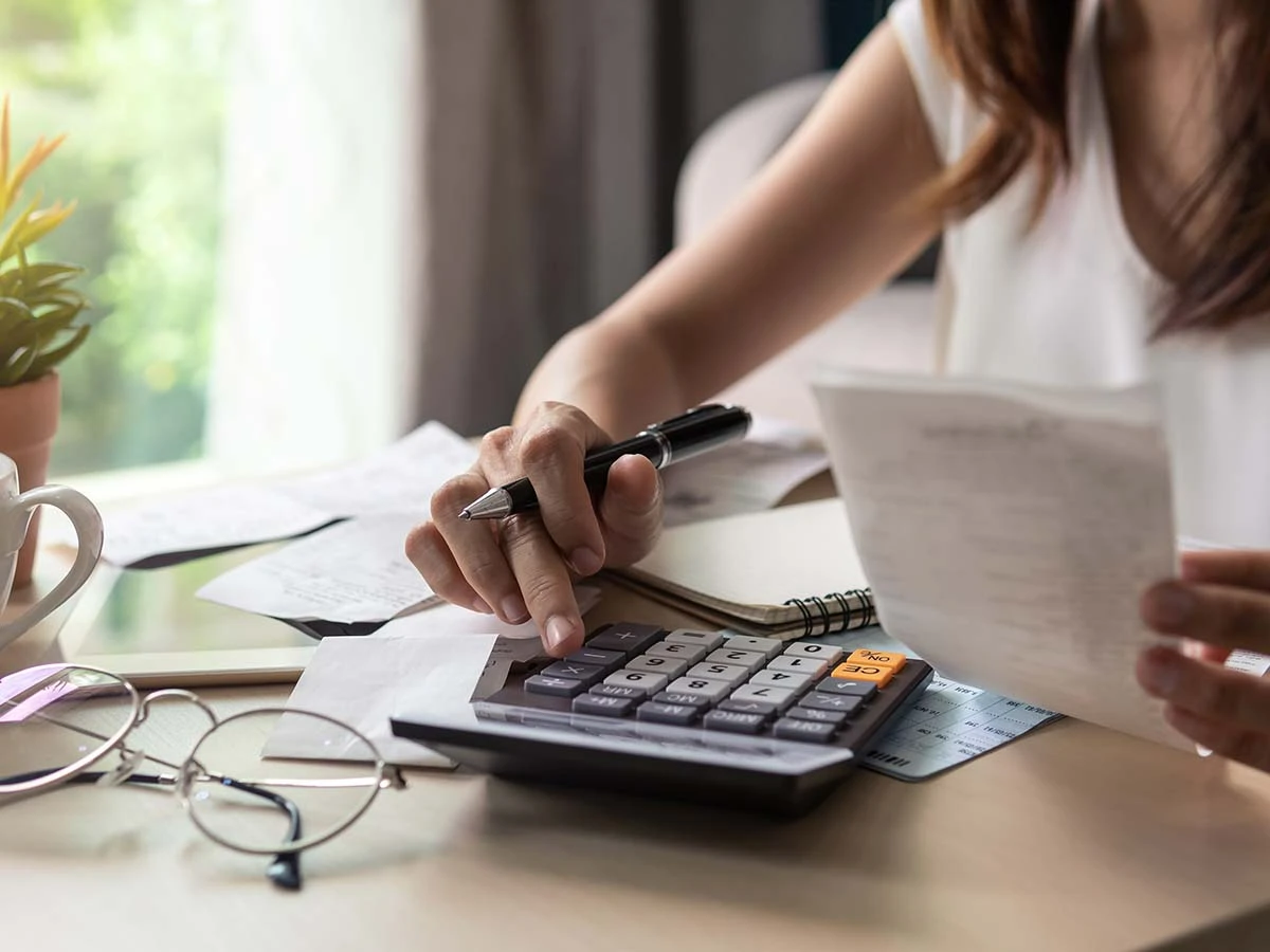 A person using a calculator and reviewing financial paperwork for international relocation budget planning.