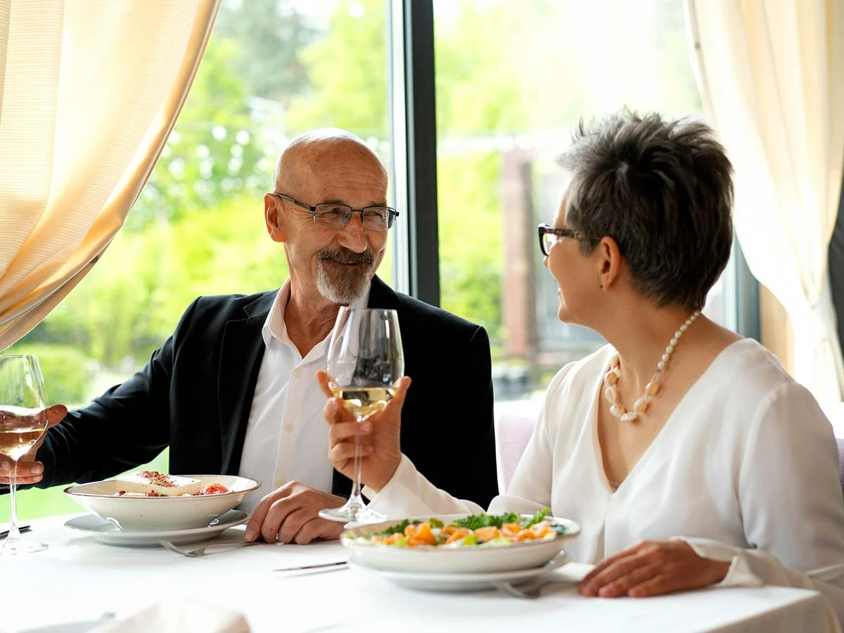 A senior couple enjoying a meal and wine at a bright tropical restaurant, highlighting the retirement lifestyle in Brazil.