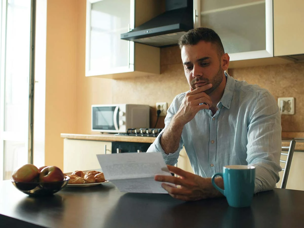 A mature man sitting at a desk thoughtfully reading a contract or official document regarding his move abroad.