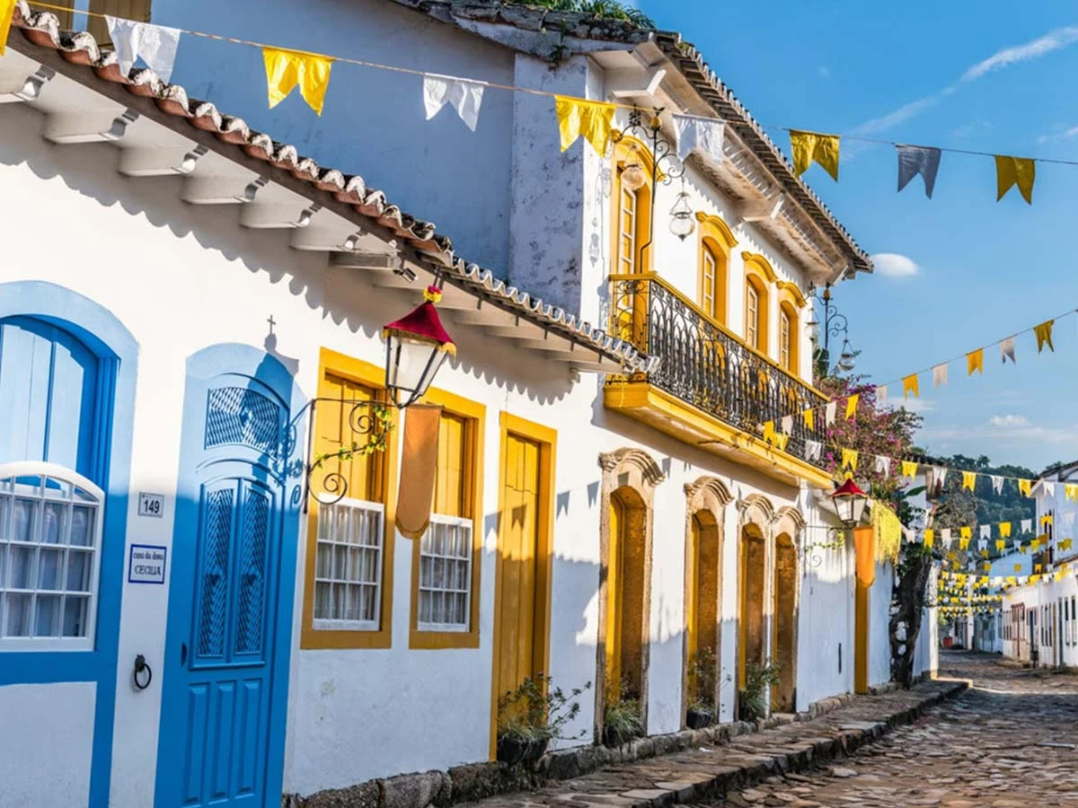 A bright, colorful street in a Brazilian colonial town with yellow and blue historic buildings and decorative flags.
