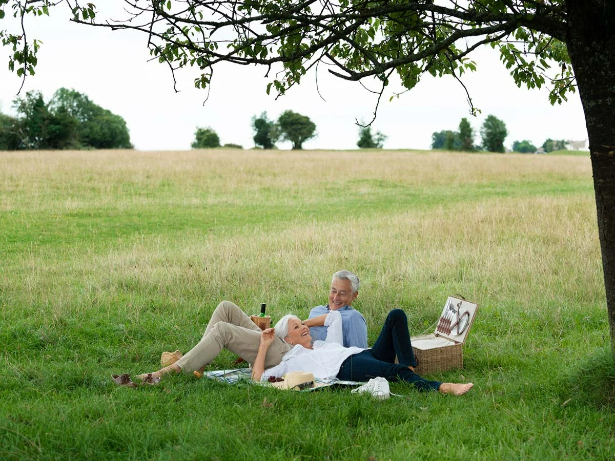 A senior retiree couple relaxing on the grass under a tree in the peaceful Brazilian countryside.