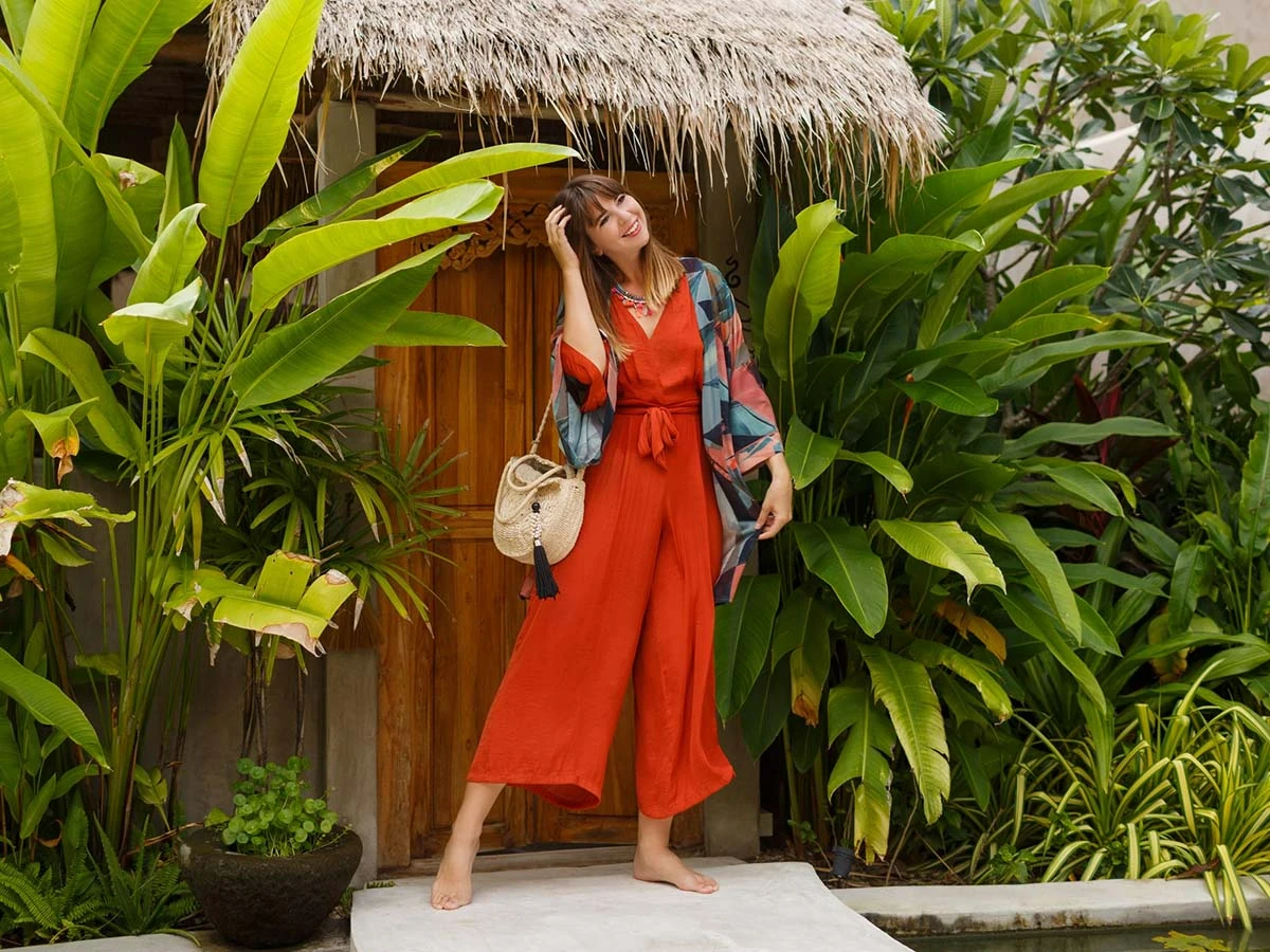 A woman in stylish red attire standing at the entrance of a lush, tropical-style home, representing the high quality of life for expats in Brazil.