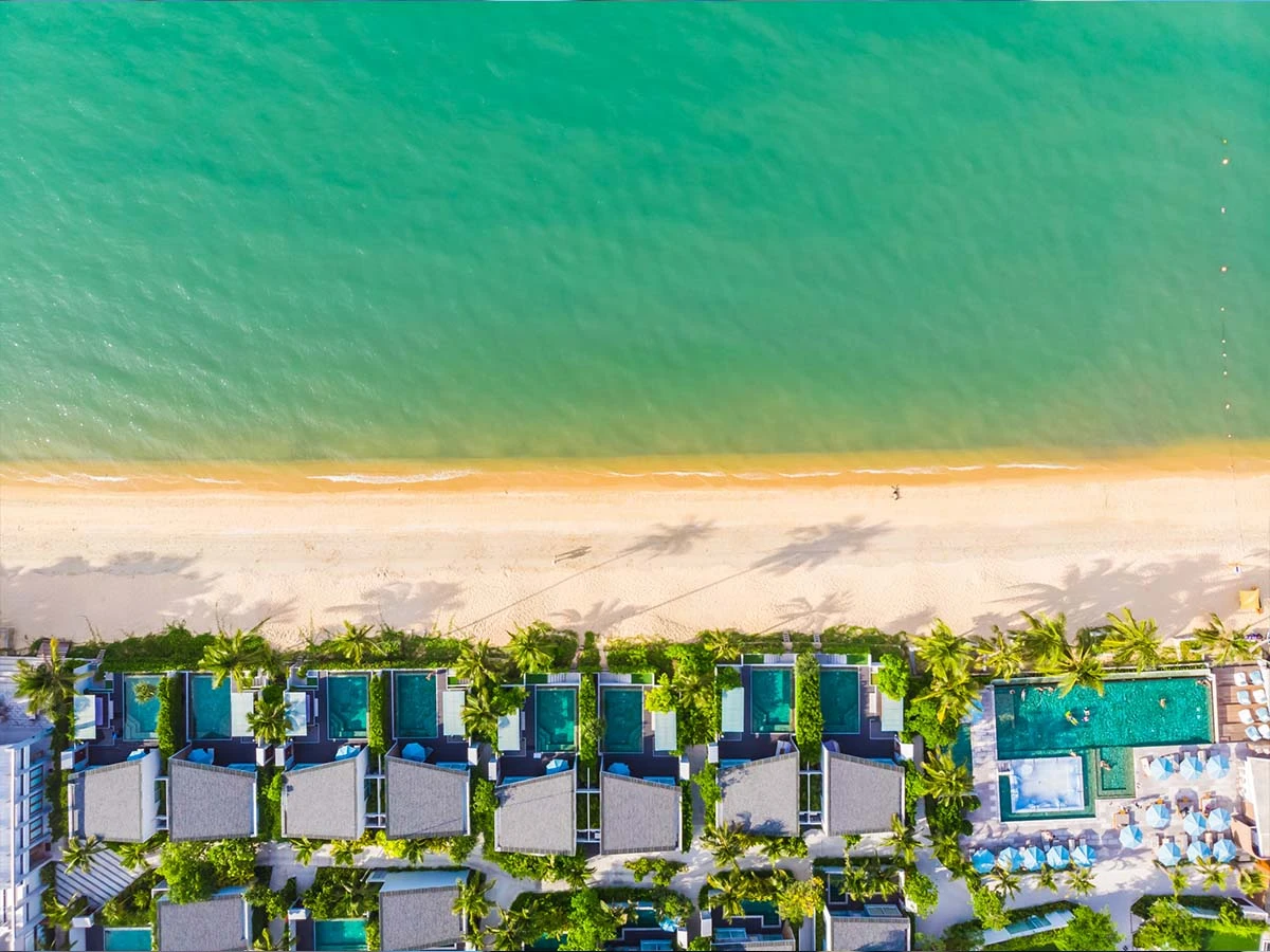 Aerial drone view of a luxury beachfront condominium complex with swimming pools and palm trees along the Brazilian coast.