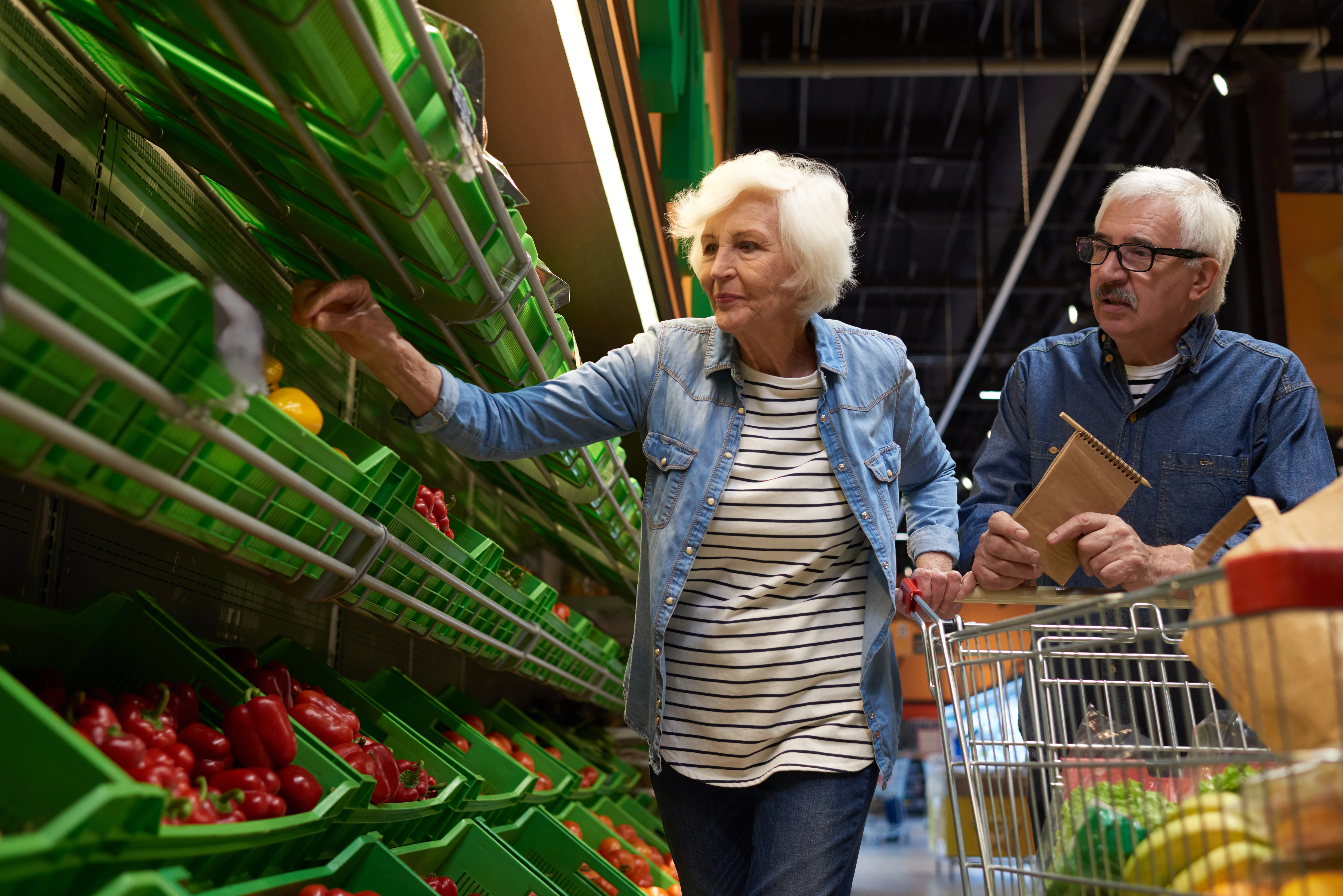 A senior couple smiling while shopping for fresh produce at a local Brazilian market, illustrating daily life for retirees.