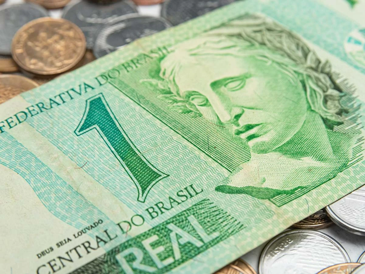 A close-up of a green one-Real Brazilian banknote and coins, representing the local tax liabilities and currency exchange for US retirees.
