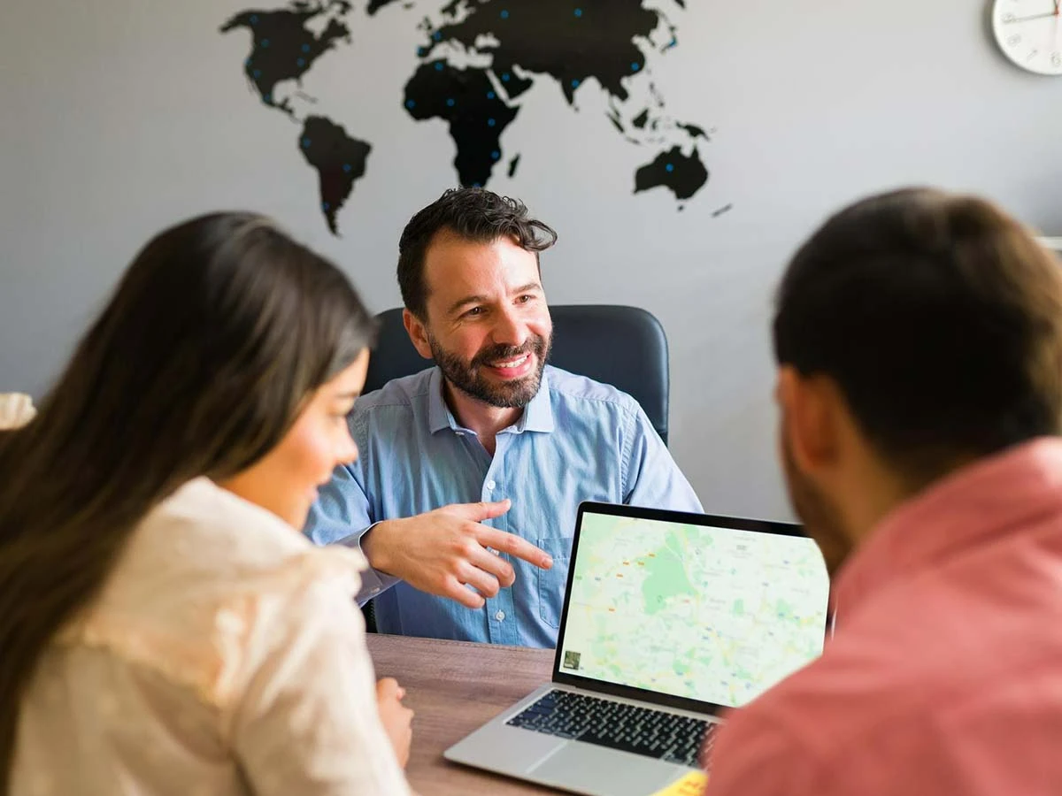 A professional consultant meeting with a couple at a desk with a laptop, discussing international relocation and expat services.