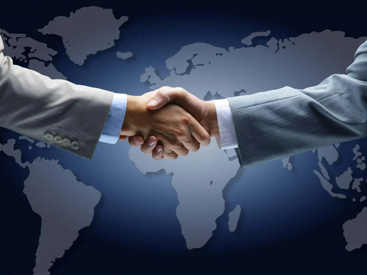 Two professionals shaking hands over a world map, symbolizing international cooperation and tax treaties for expats.