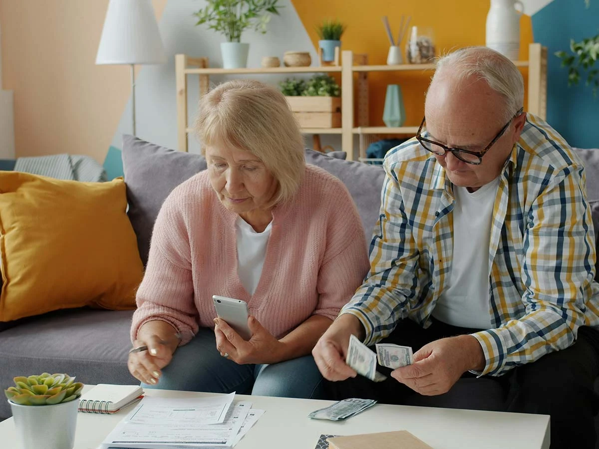 A senior couple sitting at a table counting cash and planning their monthly retirement pension budget in Brazil.