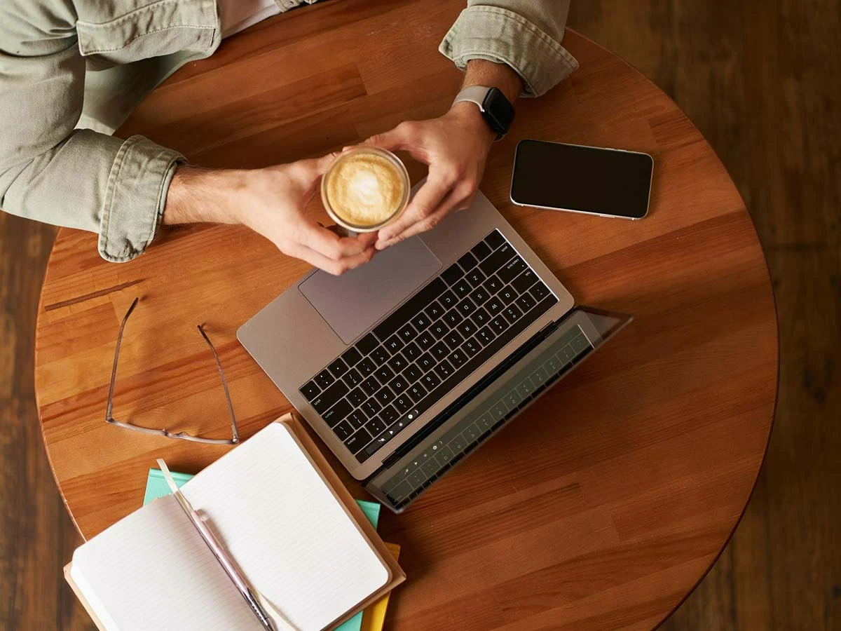 Top-down view of a person using a laptop and notepad at a wooden cafe table, symbolizing seeking advice on expat forums.