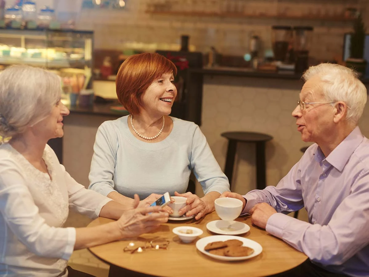 A group of senior retirees chatting over coffee in a bright Brazilian cafe, sharing tips about living abroad.