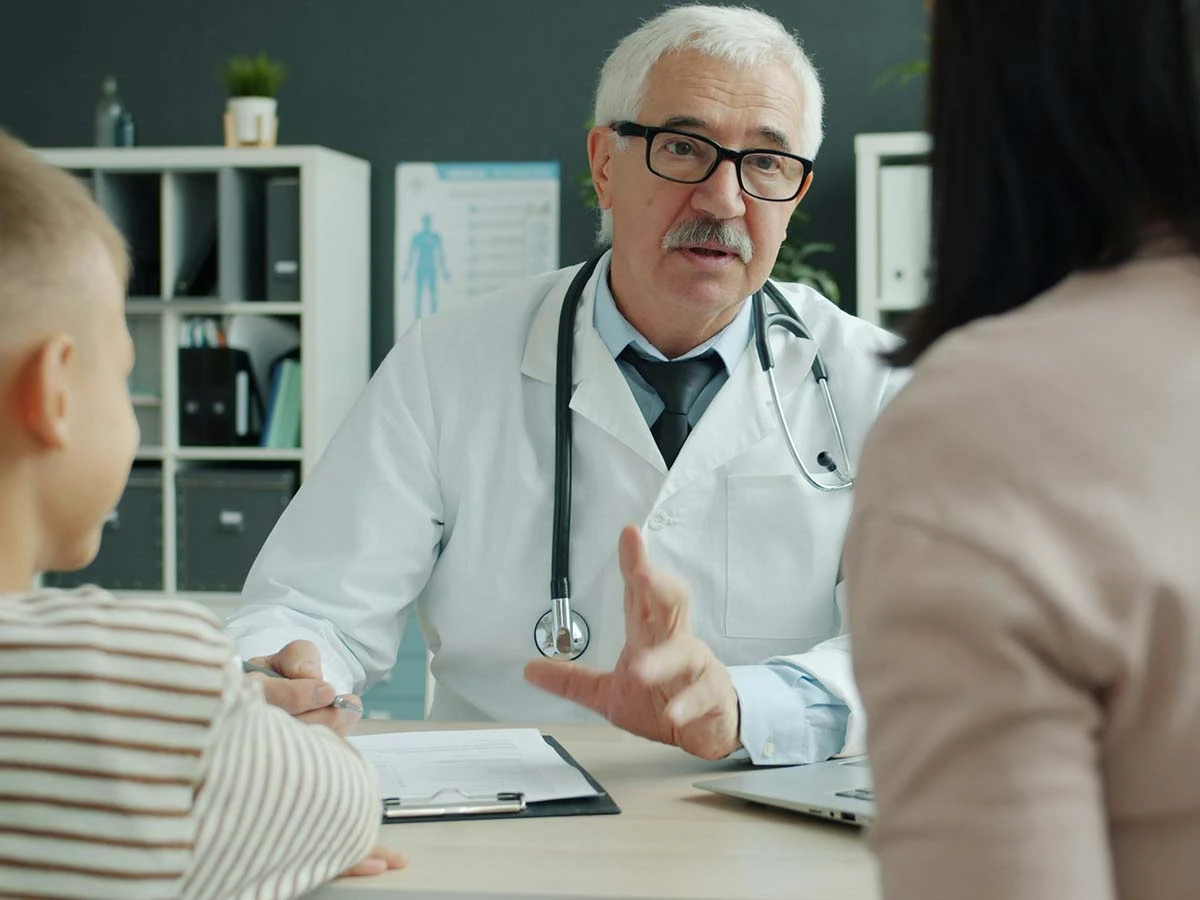 A senior doctor in a white lab coat talking to a patient, highlighting the availability of English-speaking healthcare in Brazil.