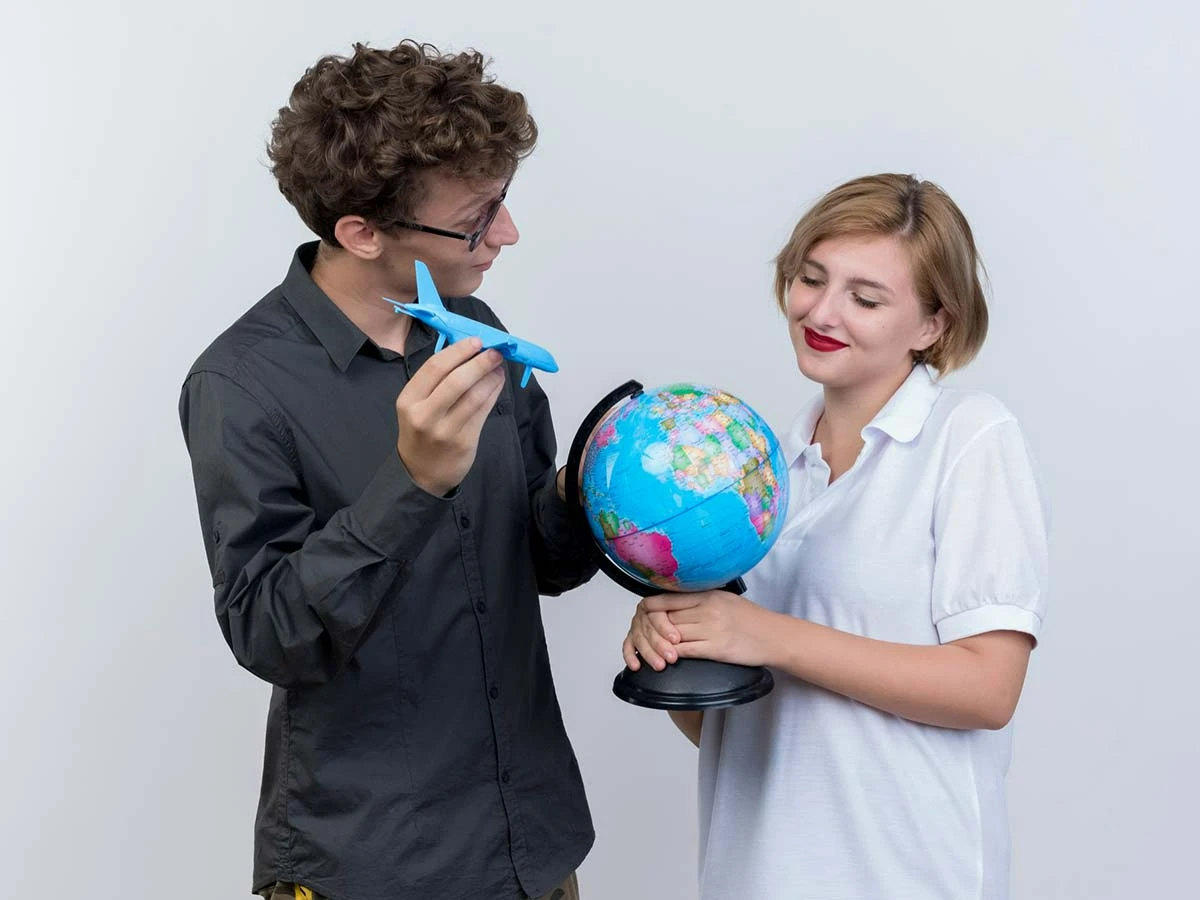 A man and woman playfully holding a globe with a toy airplane, symbolizing the decision-making process for moving to Brazil from the UK or USA.