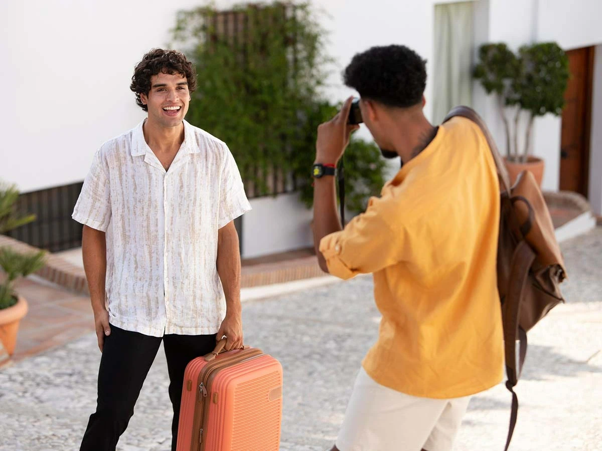 Two young men with a suitcase arriving at a bright, Mediterranean-style home in Brazil, representing the start of a new life abroad.