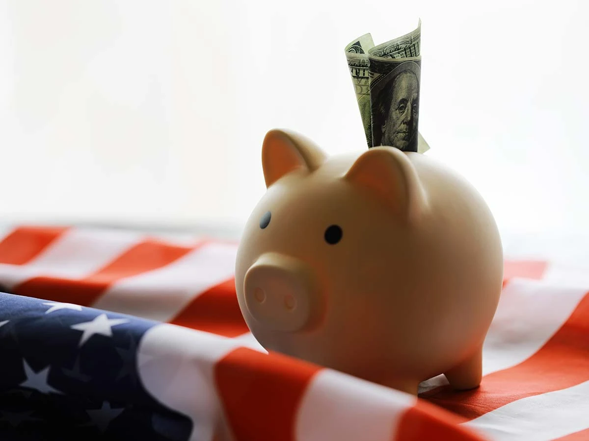 A piggy bank with a dollar bill on top of an American flag, representing retirement savings for US citizens planning a move abroad.