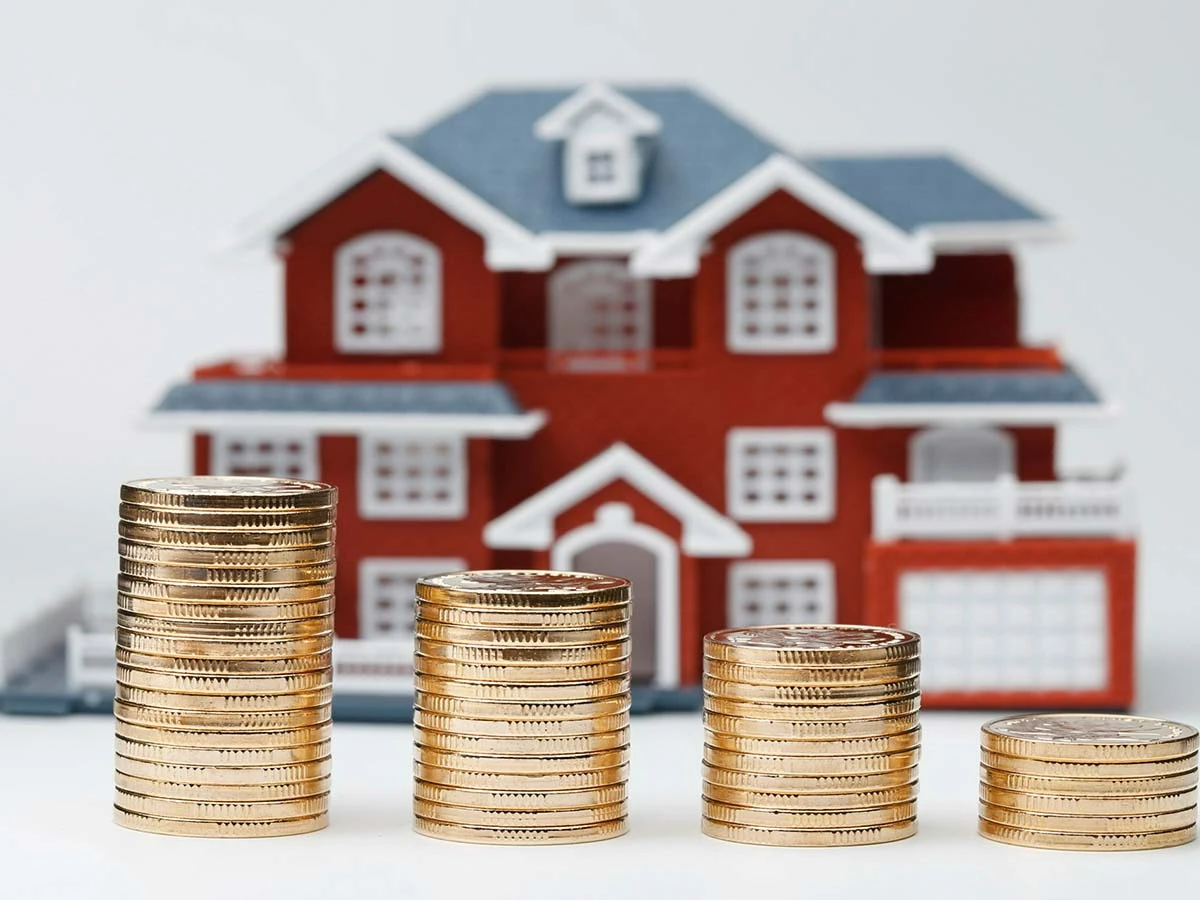 A model house next to stacks of coins, representing Brazil's IPTU property tax and real estate investment costs.
