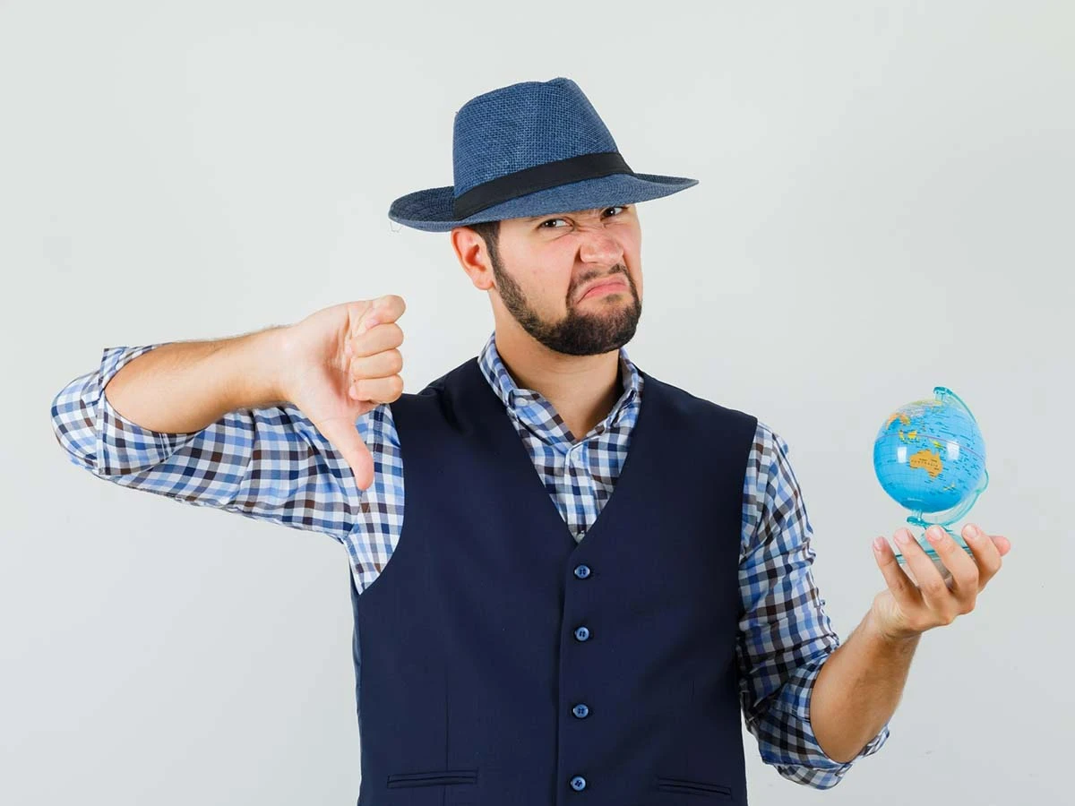A man in a hat holding a small globe and giving a thumbs down, representing the potential risks, downsides, and challenges of moving to Brazil.